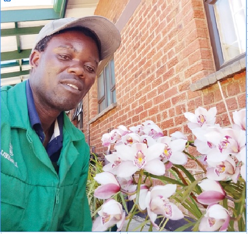 Peter Masamvu poses for a picture with some of the flowers he takes care of