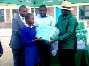 Minister of State for Provincial Affairs and Devolution, Cde Christopher Magomo (wearing a hat), and Tobacco Industry and Marketing Board (TIMB) chief executive Mr Emmanuel Matsvaire (centre) symbolically hand over sanitary wear to a Kelstone 1 Primary School learner during a donation ceremony in Guruve on Friday. Assisting is Mr Henry Pore, Ministry of Education official.Picture: Tawanda Bote