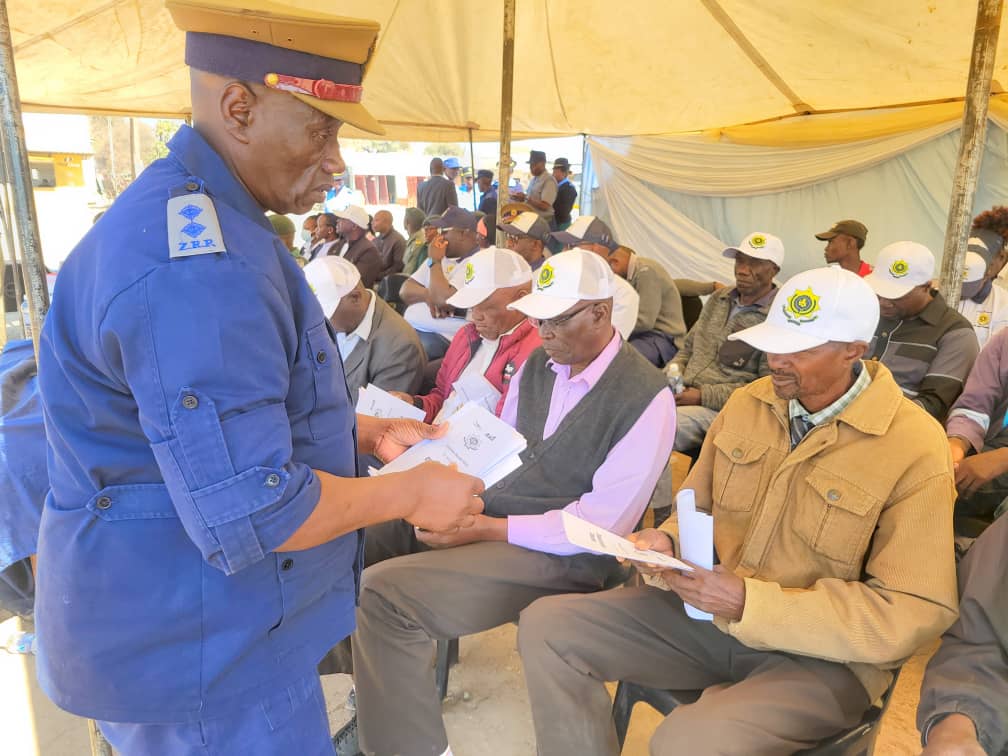 Officer in Charge of Tsholotsho Police Station, Inspector Farai Tawasika handing over pumplets to community members during ZRP Client Service Charter at Tsholotsho bus terminus on Wednesday.