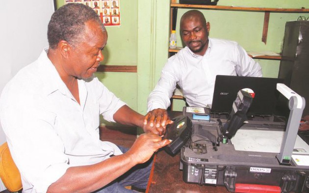 A Zimbabwe Electoral Commission official assists Mr Leonard Pundu (left) from Hatfield to have his fingerprints scanned by a BVR kit at a registration centre in Mbare
