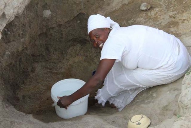 Mai Kuku using a metal plate fill one of her 12 empty plastic buckets