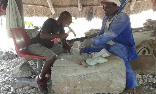 Chitungwiza Arts Centre artist Noah Limbo (right) teaches young Chris Mubayi how to carve a stone