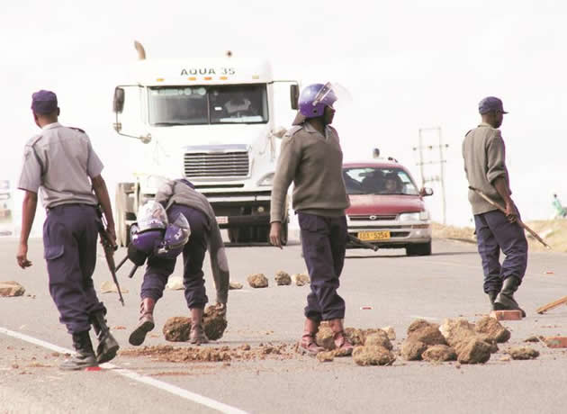 Policemen remove boulders placed by rowdy touts along Mutare Road in Zimre Park, Ruwa, on Monday