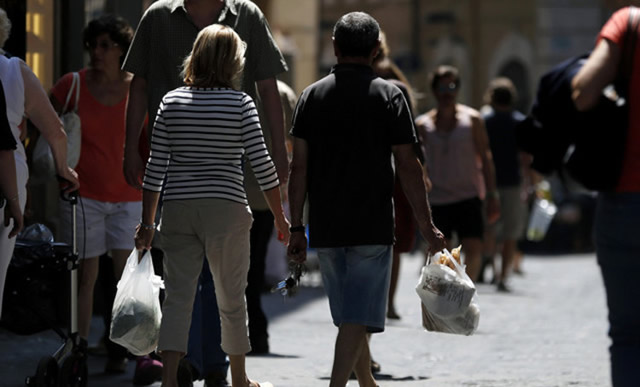 Pedestrians carry produce in shopping bags as they walk past stores in Rome. — Bloomberg