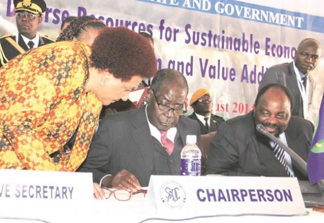Sadc Chairman and President of Zimbabwe Cde Mugabe signs one of the protocols while flanked by Sadc Executive Secretary Dr Stergomena Lawrence Tax and chairperson of the Sadc Council of Ministers Simbarashe Mumbengegwi in Victoria Falls yesterday.