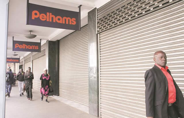 People walk past a Pelhams branch with closed roller shutters to prevent burglary after the furnisher firm sent most of its workers packing following a Supreme Court ruling allowing firms to terminate workers contracts on three months’ notice. — (Picture by Beauty Muchakazi)