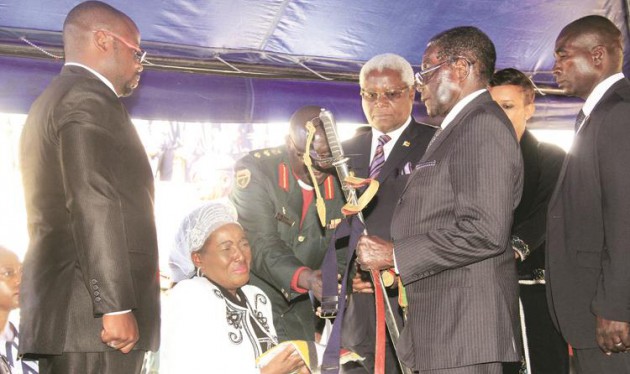 President Mugabe hands over a flag and a sword to Mrs Tapuwa Muchemwa, widow of national hero Retired Brigadier-General Felix Muchemwa, while son Fungai (left) and Home Affairs Minister Dr Ignatius Chombo (standing next to the President) look on at the National Heroes Acre in Harare yesterday. - Picture by Munyaradzi Chamalimba.