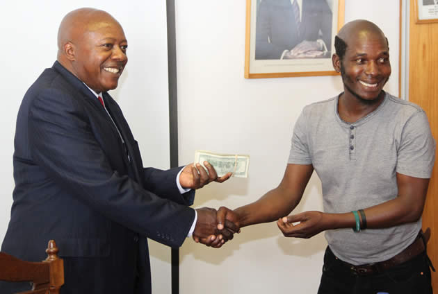 Zimpapers group chief executive Mr Justin Mutasa hands over a US$10 000 cash donation to David Mubayiwa who plays the character Sabhuku Vharazipi at Herald House in Harare yesterday