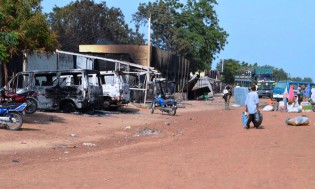 People walk past burnt vehicles and shops burnt by Boko Haram Islamists in a street of Benisheik, on September 19, 2013, after a gruesome attack by Boko Haram Islamists disguised in military uniforms in Nigeria's northeast has killed at least 87 people, a state government official said. — AFP