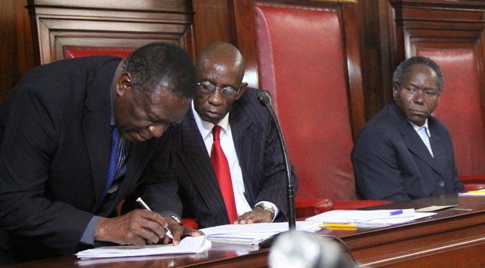 Defence Minister Emmerson Mnangagwa signs papers upon submission at the Nomination court as Registra of voters Charles Mhende and ZEC Chief elections officer Lovemore Sekeramayi looks on in Harare.